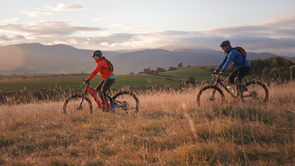 A side view of active senior couple riding bikes outdoors in forest in autumn day.