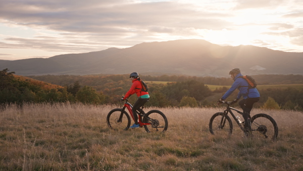 A side view of active senior couple riding bikes outdoors in forest in autumn day.