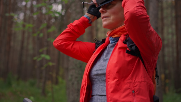 A senior woman biker putting on cycling helmet outdoors in forest in autumn day.