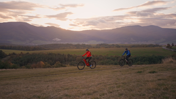 A side view of active senior couple riding bikes outdoors in forest in autumn day.