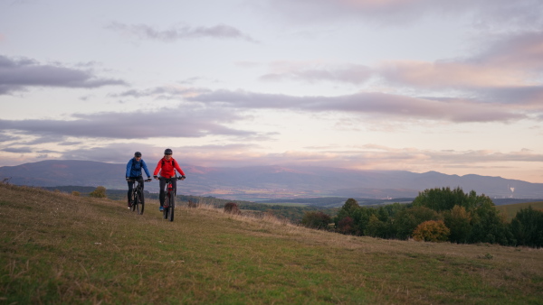 A side view of active senior couple riding bikes outdoors in forest in autumn day.