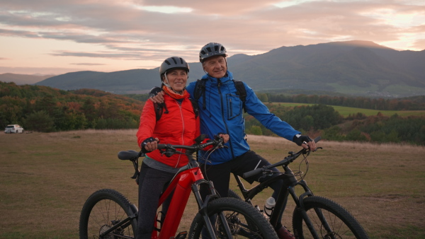 An active senior couple riding bikes outdoors in forest in autumn day.