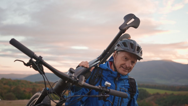 An active senior man biker carrying his bike outdoors in nature in autumn day.