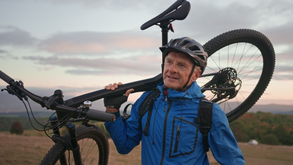 An active senior man biker carrying his bike outdoors in nature in autumn day.