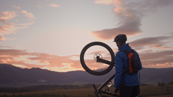 An active senior man biker carrying his bike outdoors in nature in autumn day.