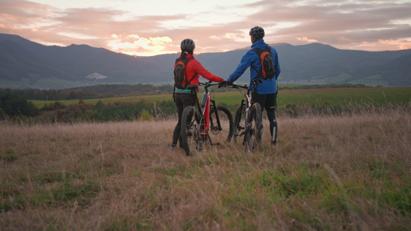 A rear view of active senior couple with bikes high fiving outdoors in forest in autumn day.