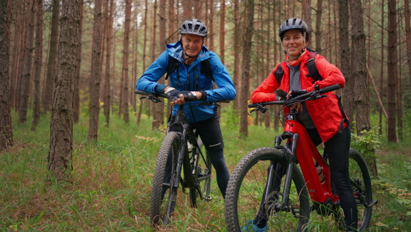 A senior couple bikers outdoors in forest in autumn day.