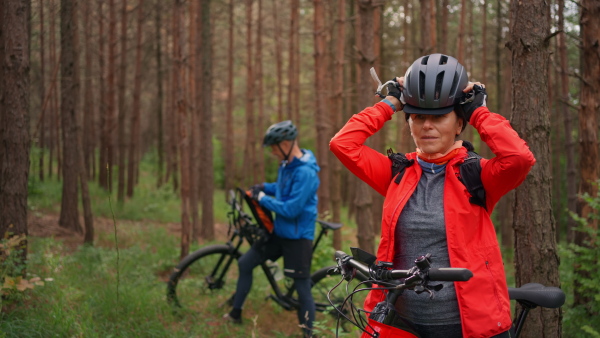 A senior couple bikers outdoors in forest in autumn day.