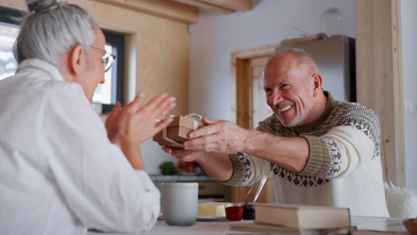 A senior woman getting present from her husband at home during breakfast.