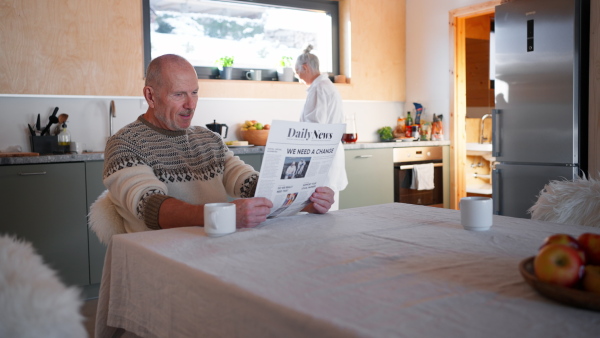 A senior couple on holiday in cabin, resting reading newspaper in kitchen.