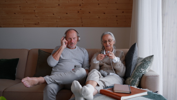 A senior Couple Sitting on Sofa, with the Woman Knitting and the Man Listetning the Music.