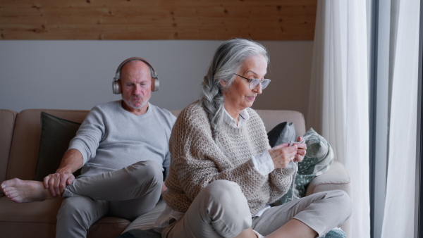 A senior Couple Sitting on Sofa, with the Woman Knitting and the Man Listetning the Music.