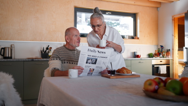 A senior couple on holiday in cabin, resting reading newspaper in kitchen.