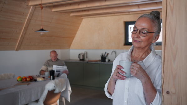 A senior couple on holiday in cabin, resting reading newspaper and drinking tea in kitchen.