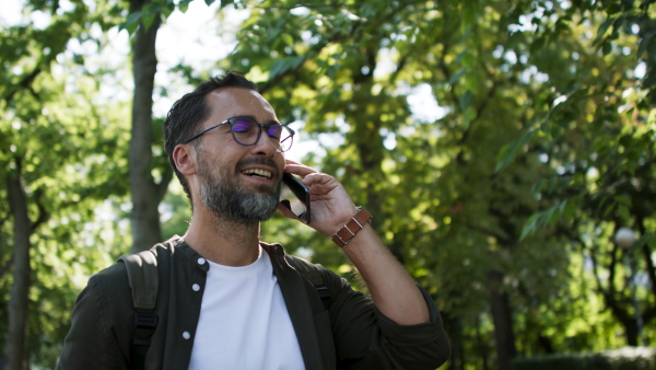 A handsome mature man walking and talking on phone in park.