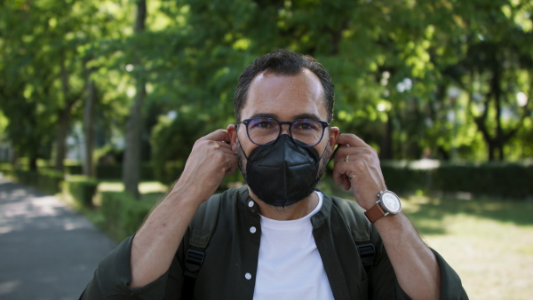 A handsome mature man putting off face mask in park, coronavirus concept.