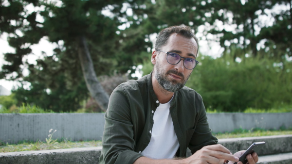 A dandsome mature man sitting and using phone in park.