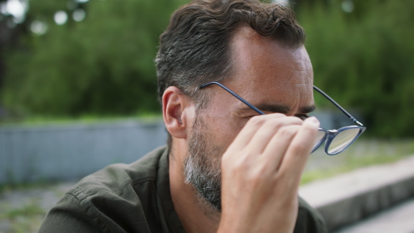 A close-up of handsome mature man putting on glassesy and looking at camera outside.