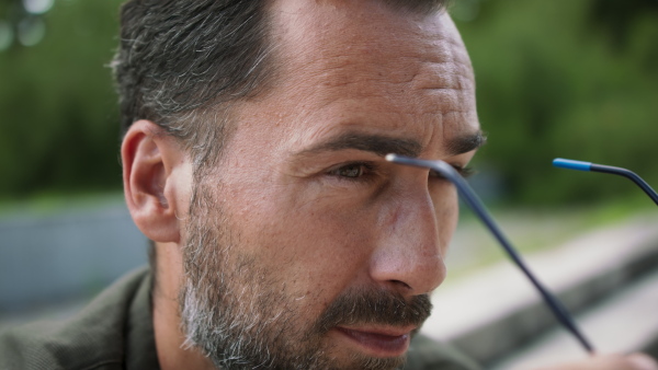 A close-up of handsome mature man putting on glassesy and looking at camera outside.