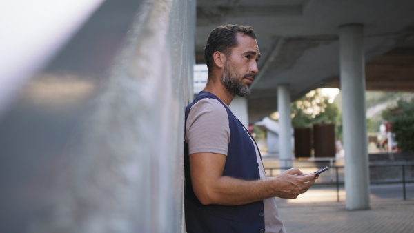 A handsome mature man with smartphone waiting at station.