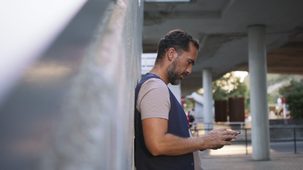 A handsome mature man with smartphone waiting at station.