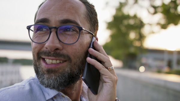 A happy mature man using smartphone and resting outdoors in riverside.