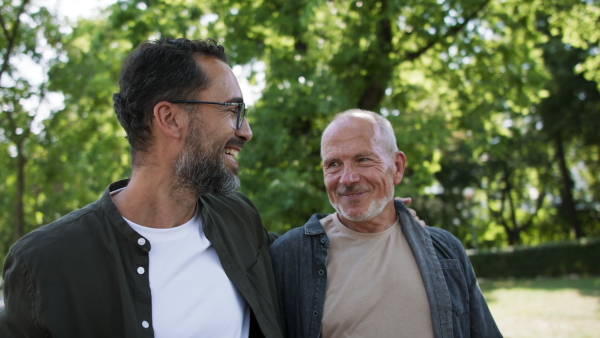 A senior man with his mature son walking and talking outdoors in park.