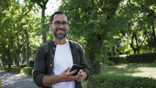 A handsome mature man walking and talking on phone in park.