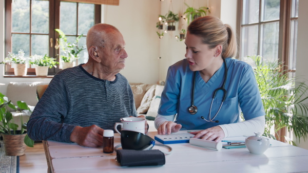 A happy healthcare worker or caregiver visiting senior woman indoors at home, talking and explaining dosage of pills.