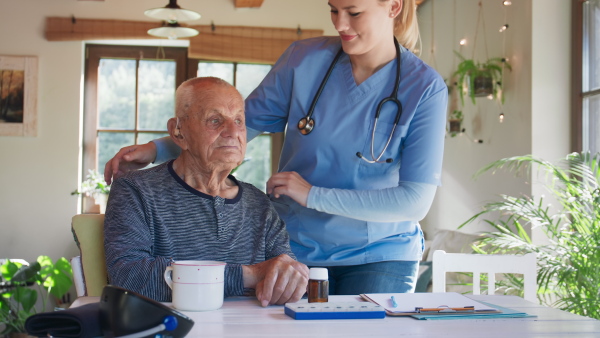 A happy healthcare worker or caregiver visiting senior woman indoors at home, talking.