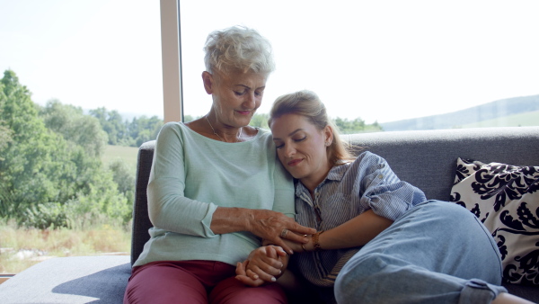 An adult daughter embracingwith happy senior mother indoors at home.