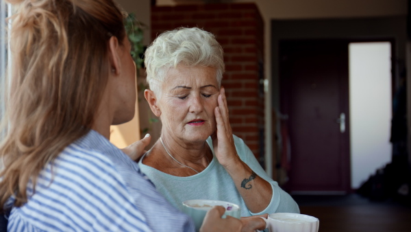 An adult daughter consoling unhappy senior mother and supporting her in struggle indoors at home.