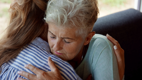 An adult daughter consoling unhappy senior mother and supporting her in struggle indoors at home.