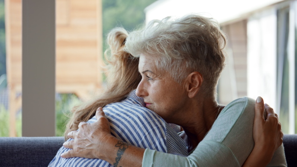 An adult daughter consoling unhappy senior mother and supporting her in struggle indoors at home.