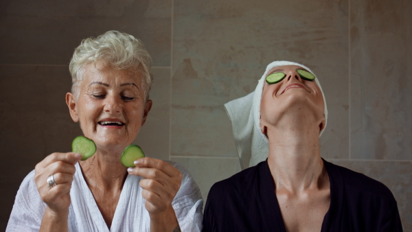 A happy senior mother in bathrobe with adult daughter indoors at home, selfcare concept.