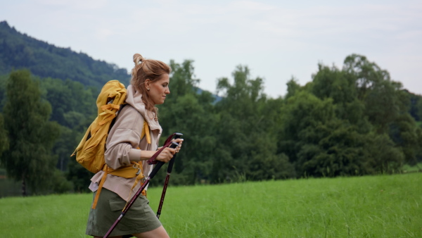 A mid adult woman with trekking poles hiking outdoors in nature.