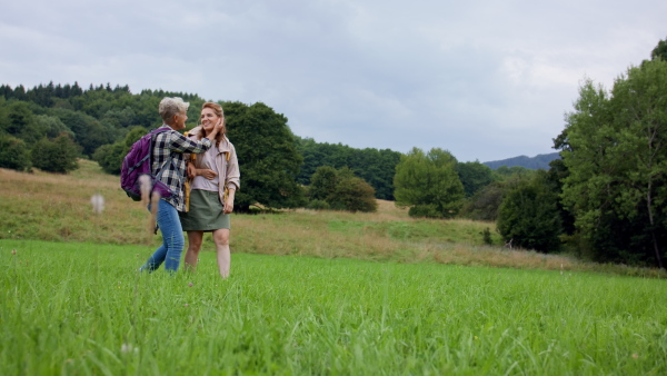 A low angle view of mid adult woman with trekking poles hiking with active senior mother outdoors in nature.