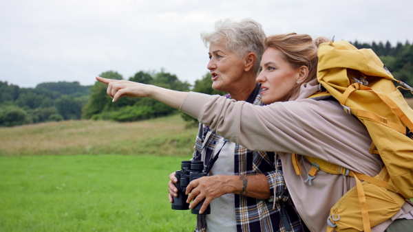 A happy senior mother hiker with adult daughter looking through binoculars outdoors in nature