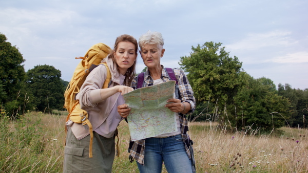 A happy senior mother hiker with adult daughter looking through binoculars outdoors in nature