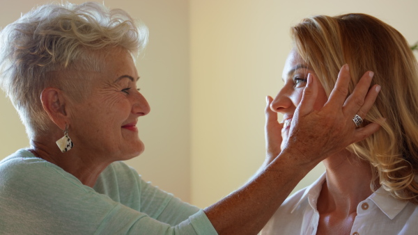 A happy senior mother kissing her adult daughter on forehead.