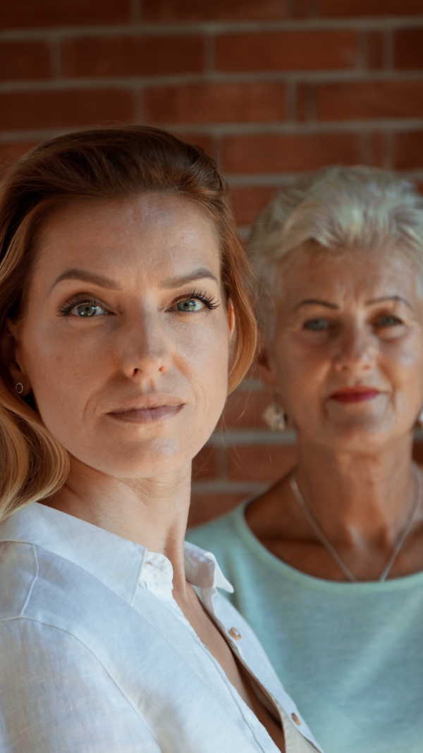 A vertical footage of senior mother looking at her adult daughter indoors at home. Selective focus.