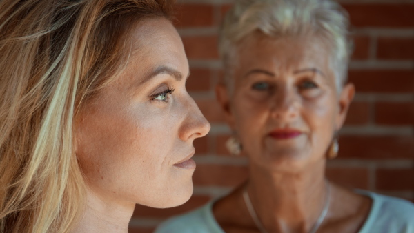 A senior mother looking at her adult daughter indoors at home. Selective focus.