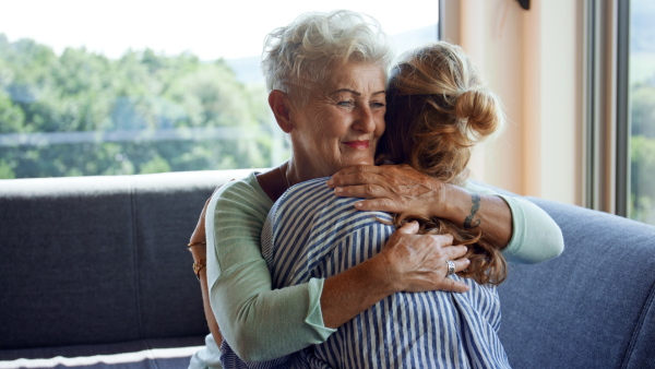 A rear view of adult daughter hugging happy senior mother indoors at home.