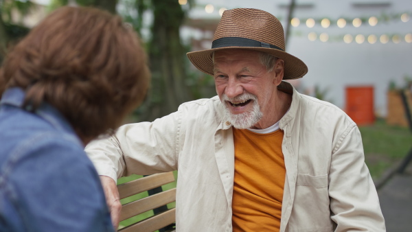 A happy senior couple sitting on bench and talking outdoors in town.