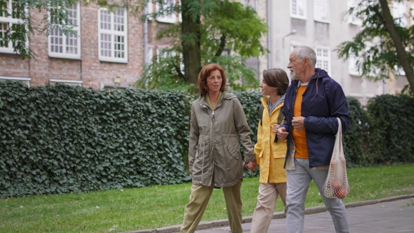 Happy grandparents with a preteen grandddaughter walking together ourtdoors in town street