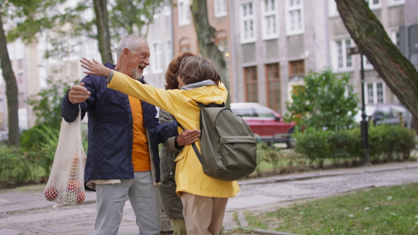 Happy grandparents with a preteen grandddaughter hugging together ourtdoors in town street