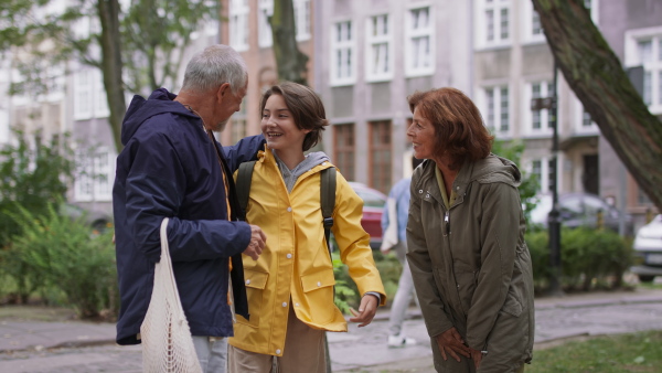 Happy grandparents with a preteen grandddaughter walking together ourtdoors in town street