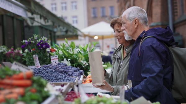 A happy senior couple tourists buying fruit outdoors on market in town.