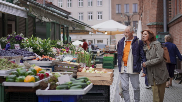 A happy senior couple tourists buying fruit outdoors on market in town.