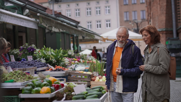 A happy senior couple tourists buying fruit outdoors on market in town.